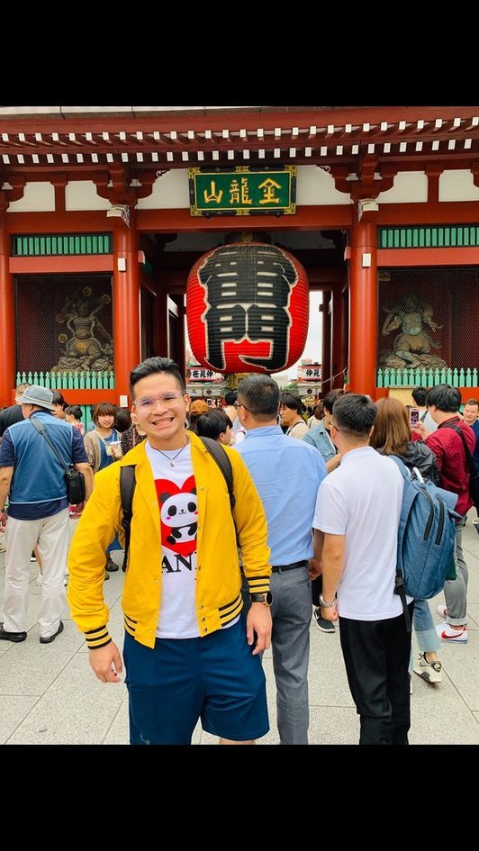 Nico in a yellow jacket and glasses smiling under the giant red lantern at the Kaminarimon gate of Senso-ji in Asakusa.