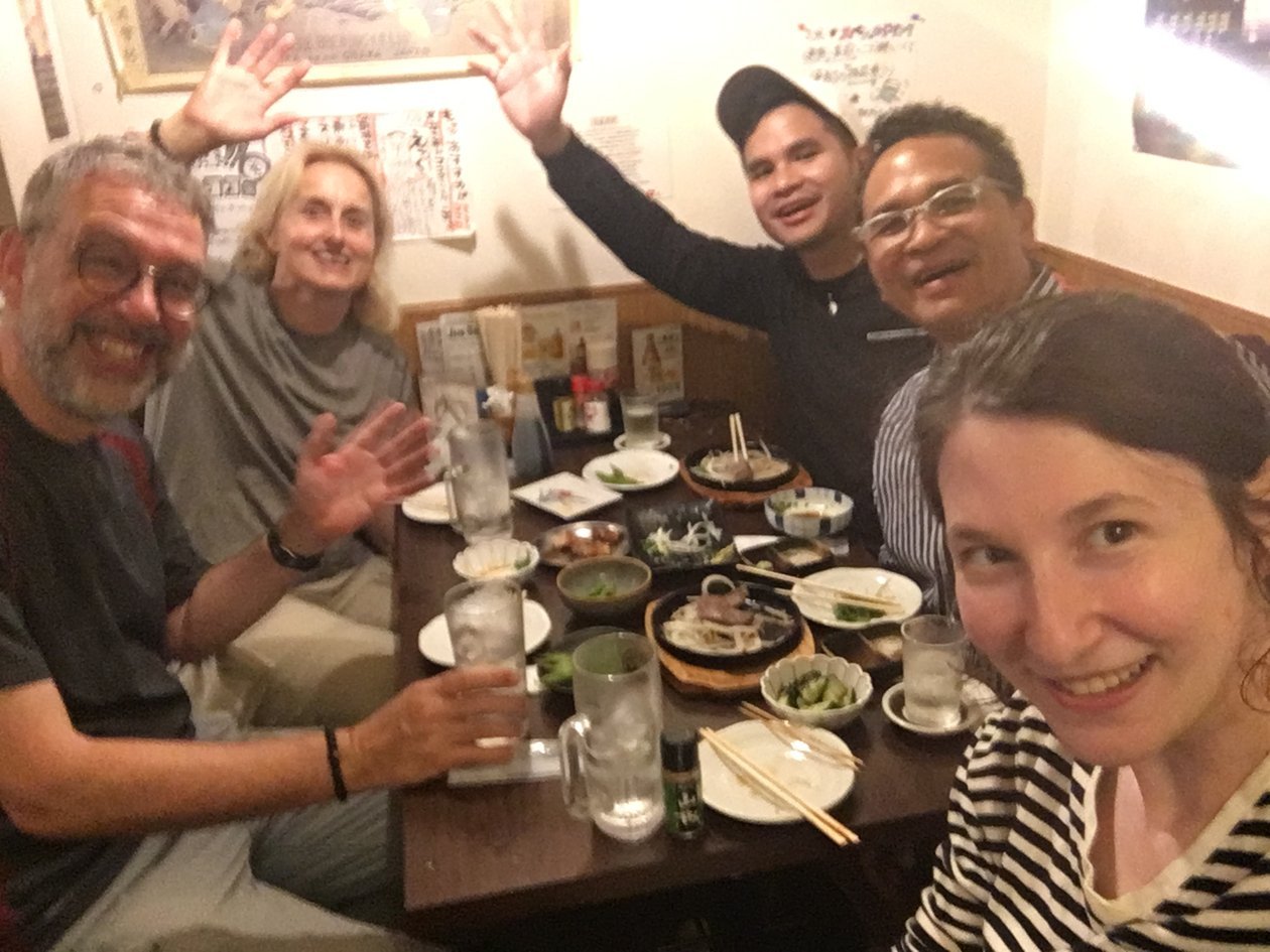 Nico and Dad squeezed into an izakaya booth in Kyoto with three other people, waving over a table of noodles, small plates, and iced drinks.