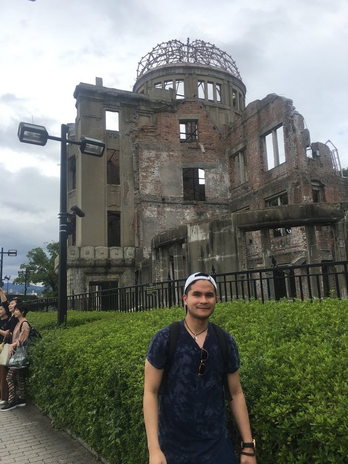 Nico in a backwards white cap and blue shirt standing in front of the ruined Atomic Bomb Dome in Hiroshima.