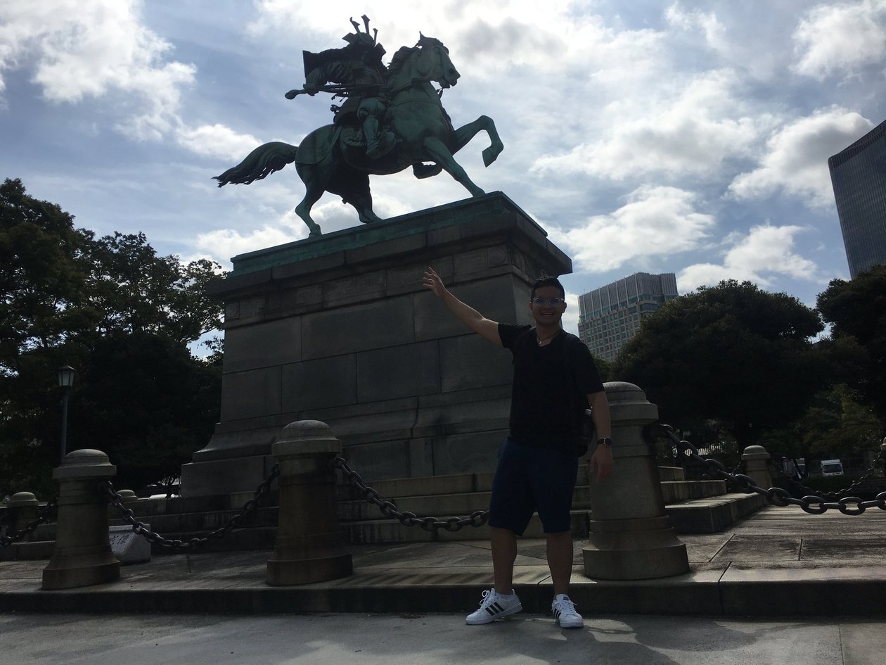 Nico in a black t-shirt pointing up at the bronze statue of a samurai on a rearing horse.