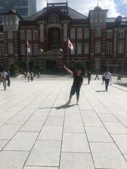 Dad jumping with both arms up in the stone plaza in front of the red-brick Tokyo Station.