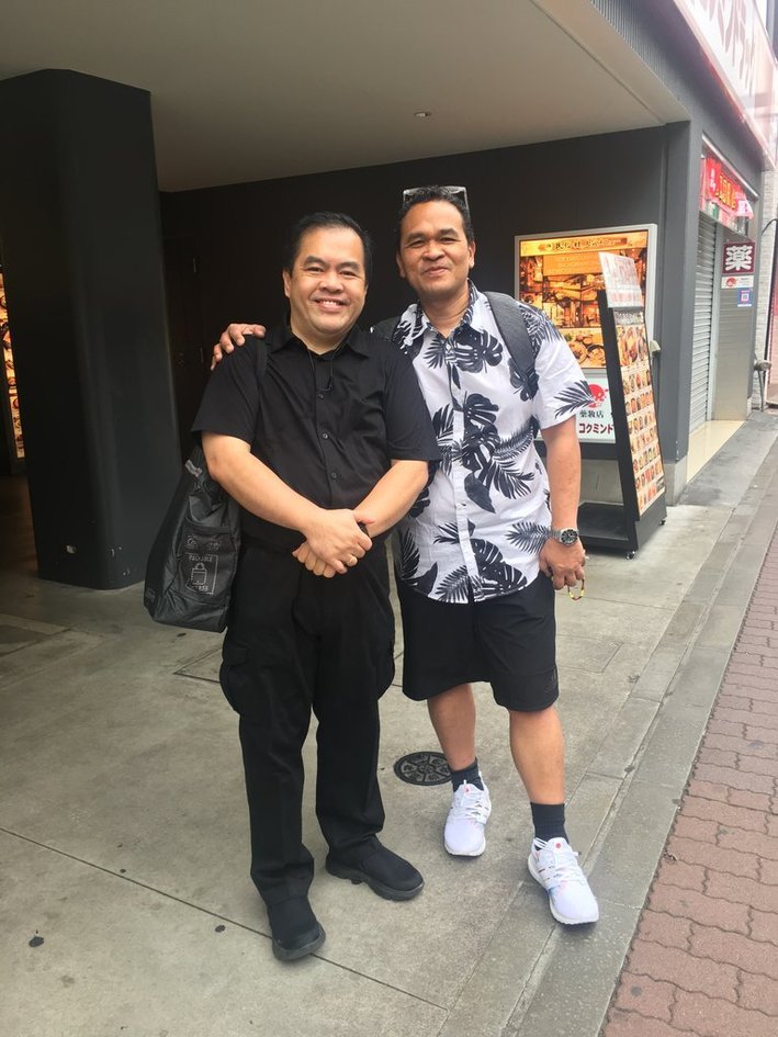 Dad’s friend in a black shirt and Dad in a black-and-white leaf shirt, standing together outside a restaurant in Japan.