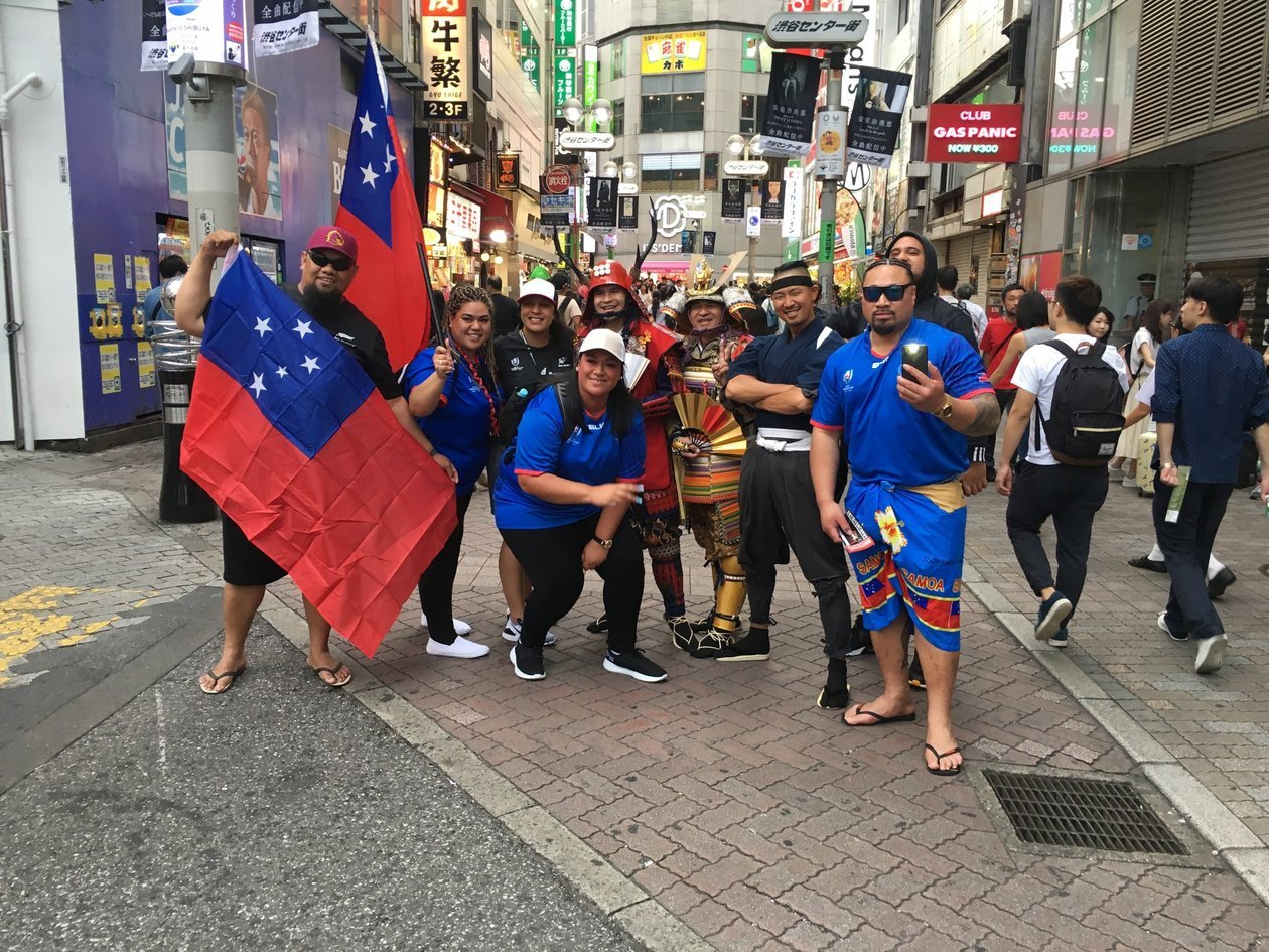 A Samoa rugby group posing in Shibuya with two samurai performers, one person holding the Samoa flag.