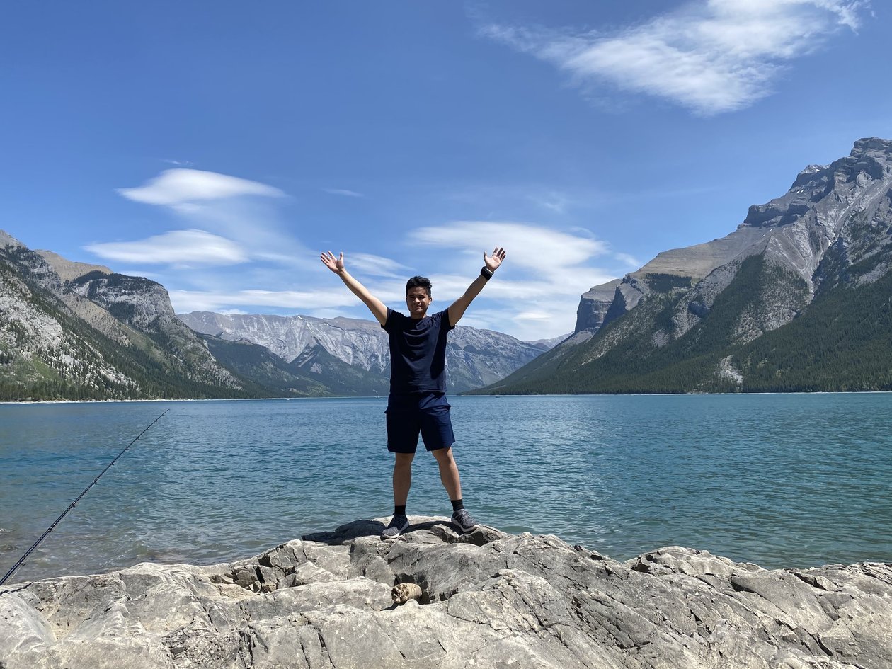 Standing on the rocky shore of Lake Minnewanka with arms outstretched