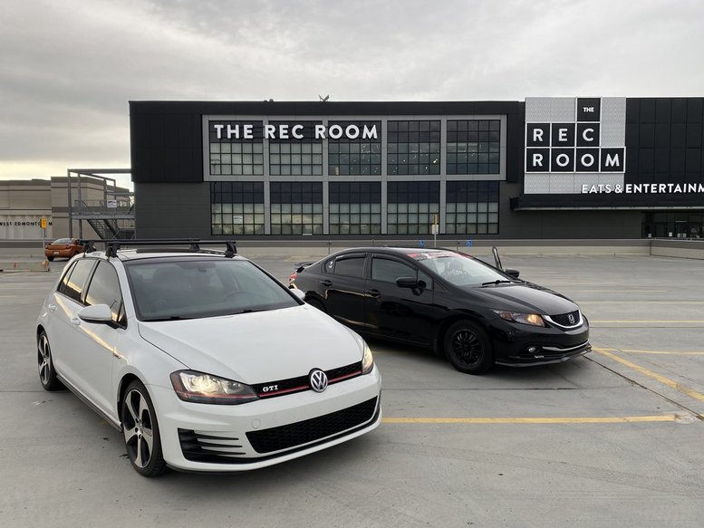 A white VW GTI and a black Honda Civic parked in an empty parking lot outside The Rec Room