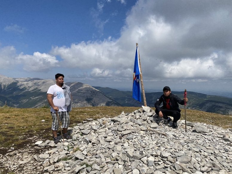 Charles and Christian sitting at the rocky summit with a flag