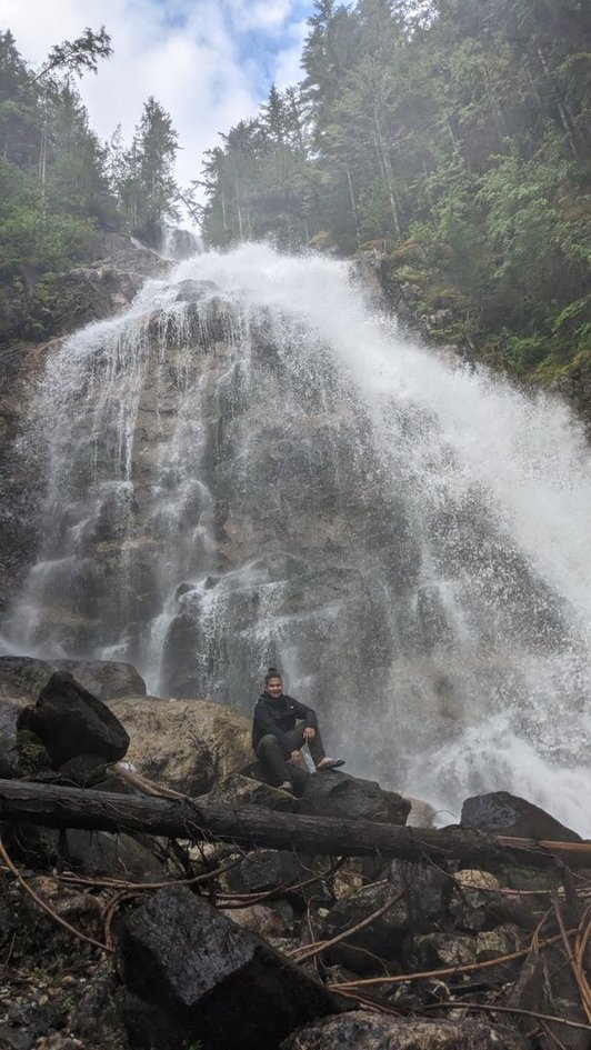 Nico sitting on the rocks by a massive waterfall