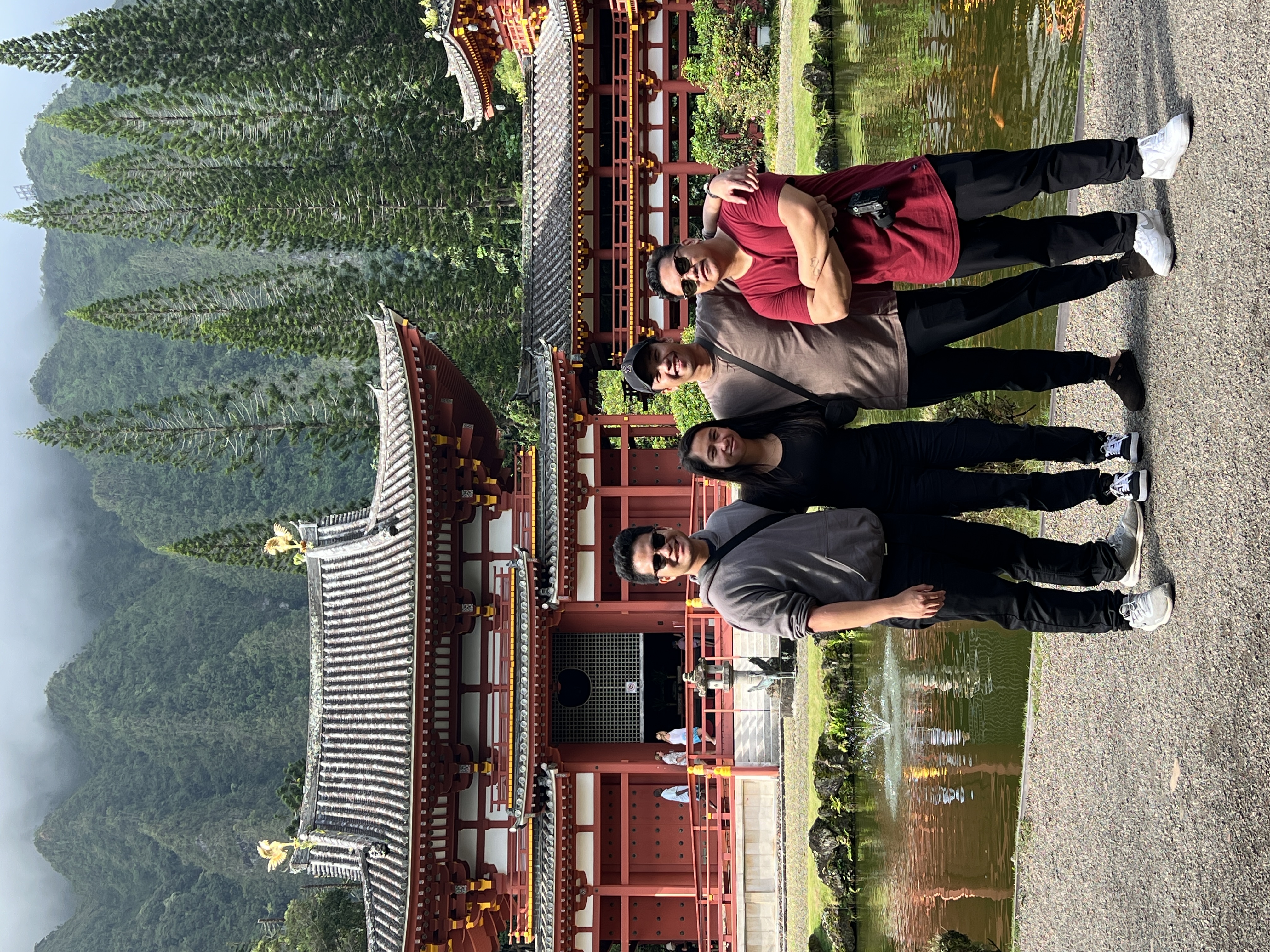 Four people posing beside the reflecting pond at Byodo-In, the temple mirrored in the water.