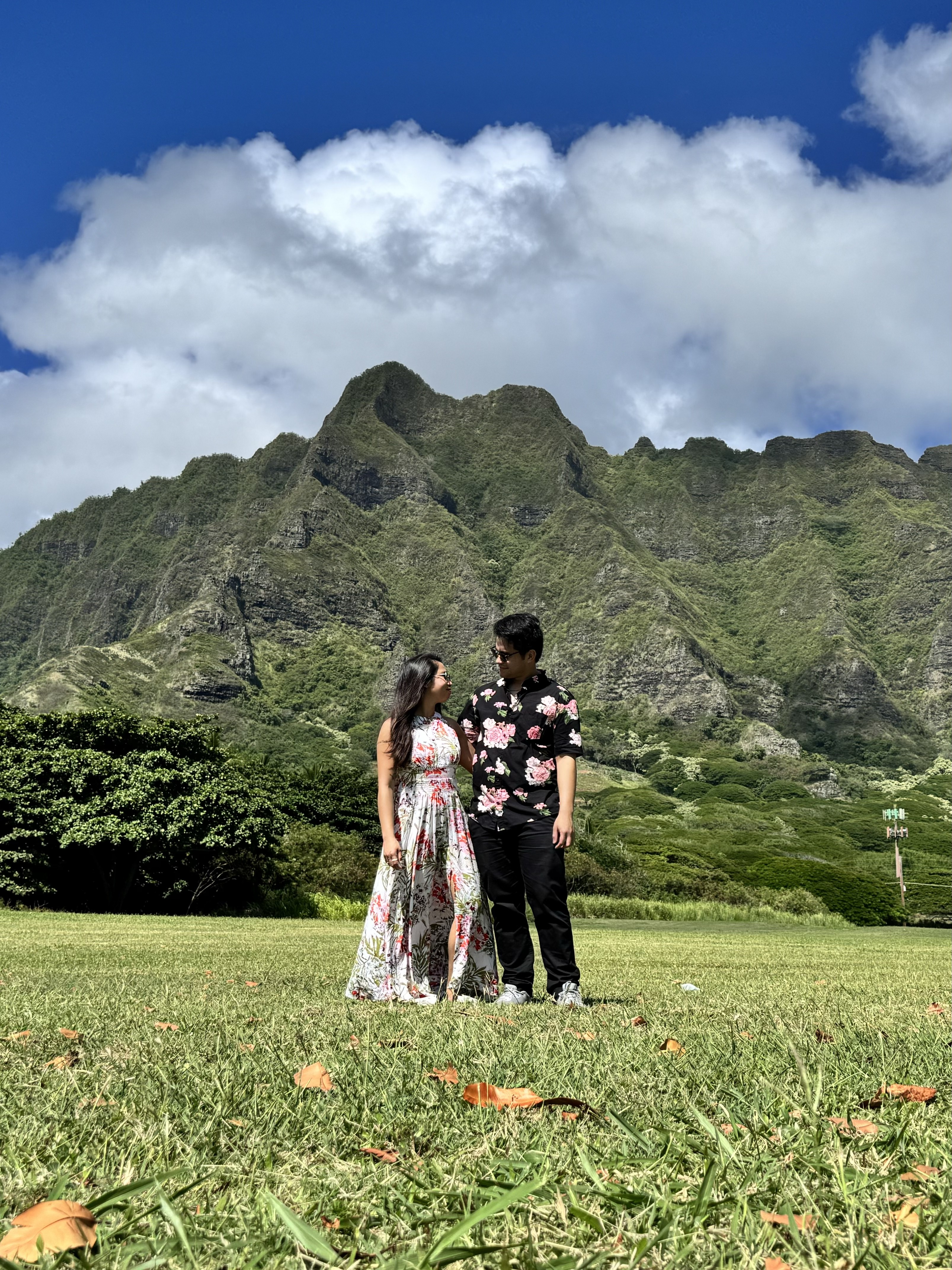 Sarah and Nico standing in the grass at Kualoa, looking at each other, the Koʻolau cliffs behind them.