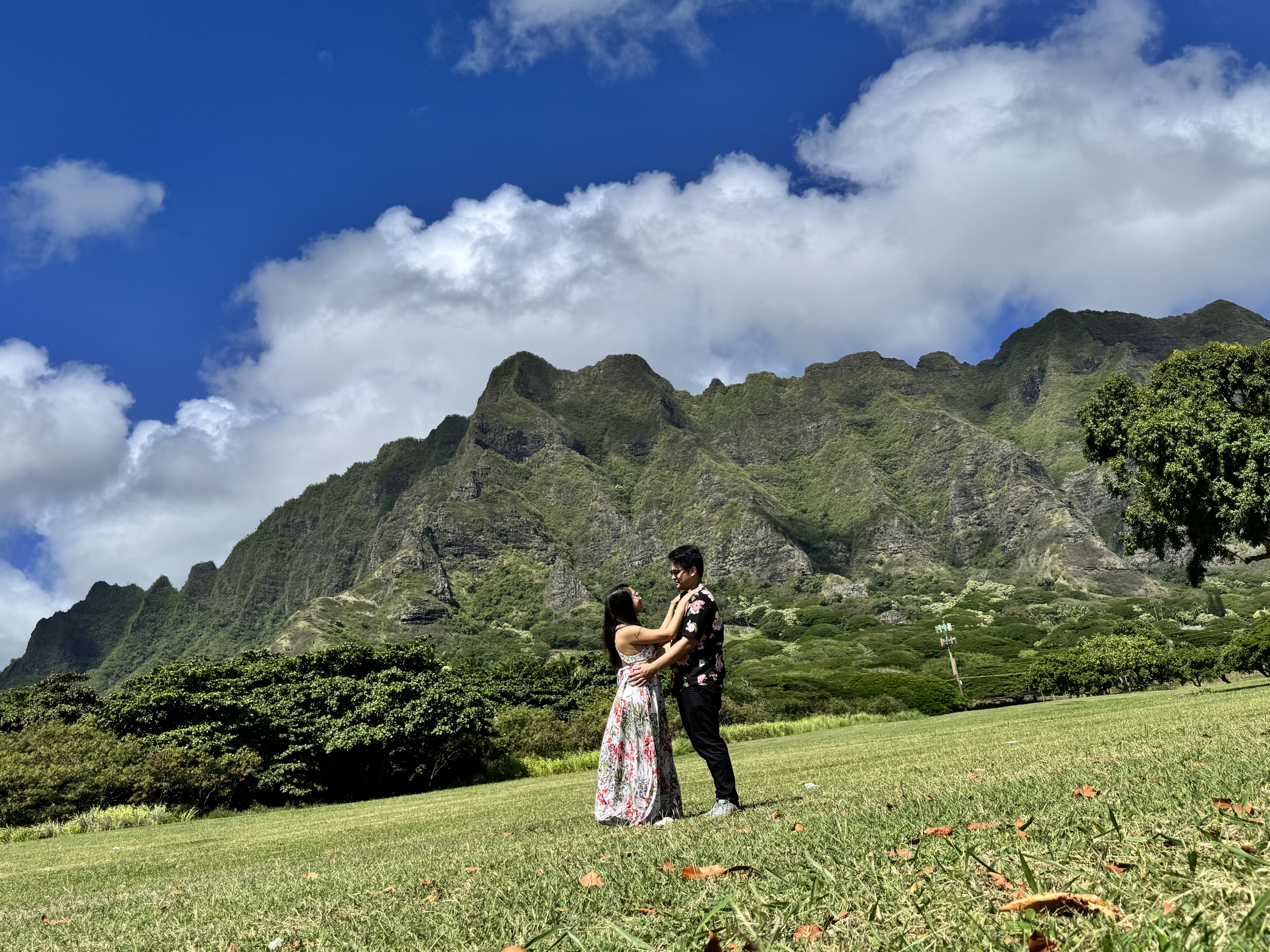 Sarah and Nico embracing in the field at Kualoa, her hand on his shoulder, the mountains behind them.
