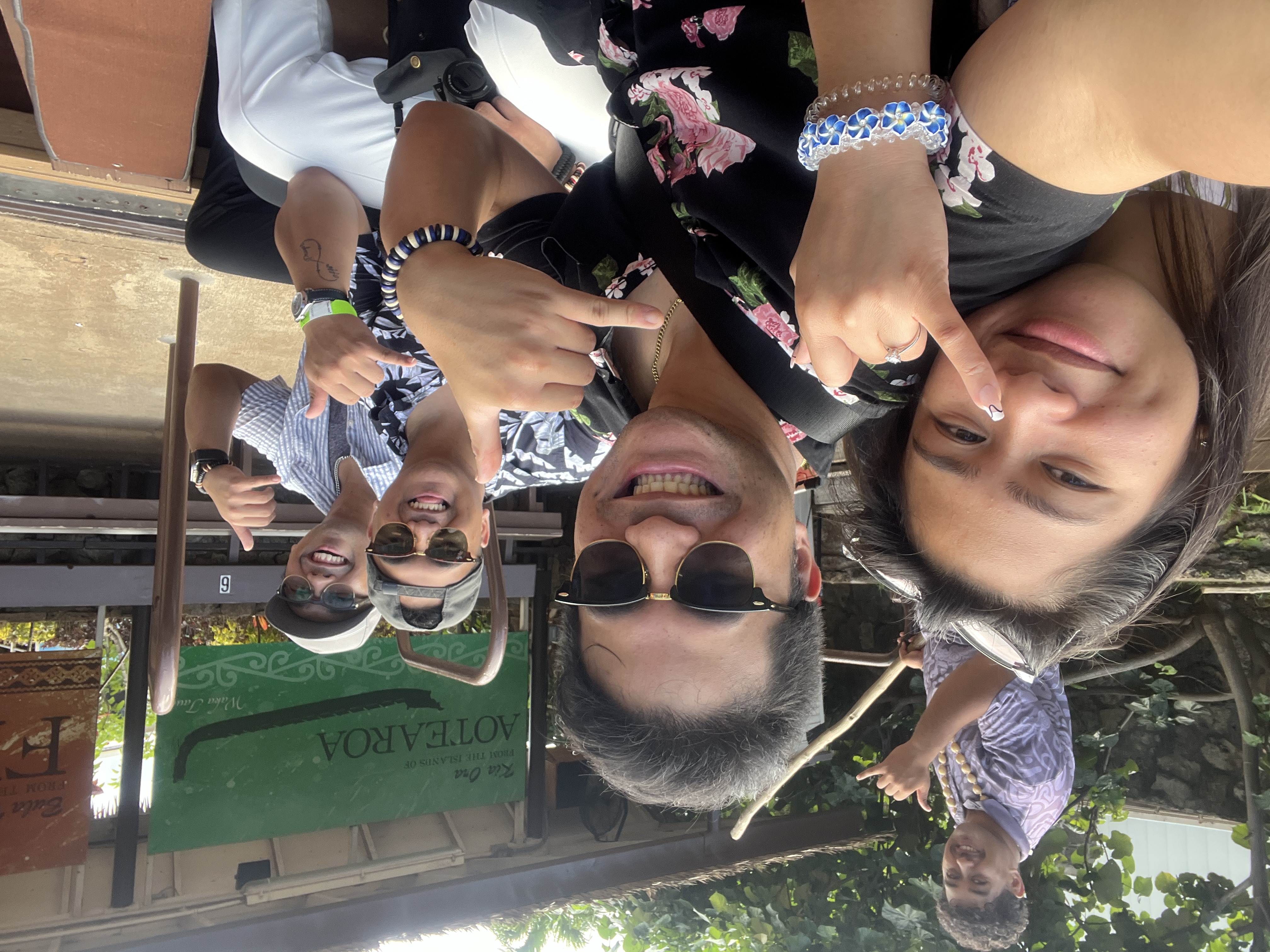 A canoe selfie at the Aotearoa village: Sarah, Nico, two friends, and a guide in a purple shirt making a shaka under the Kia Ora sign.