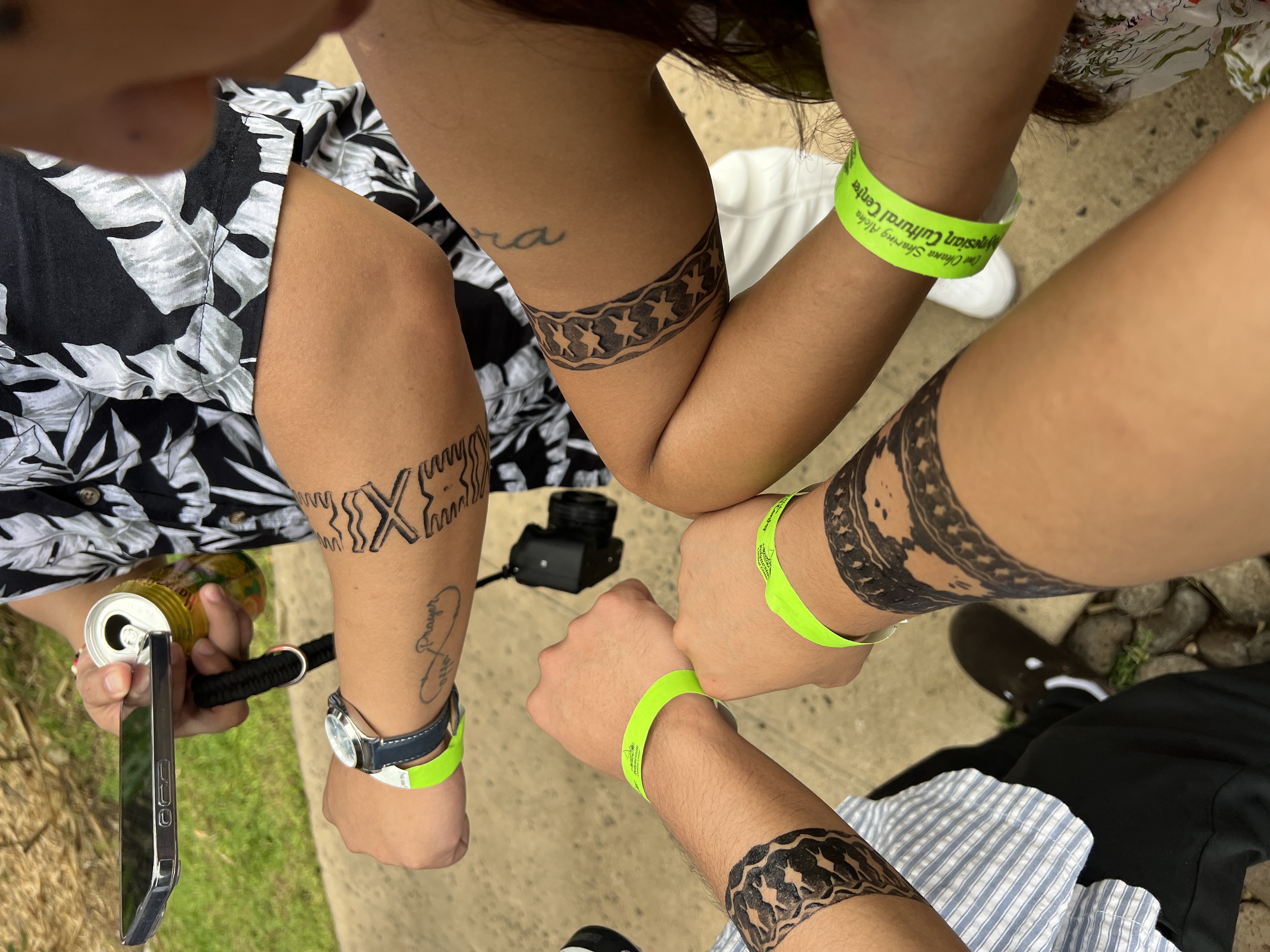 Forearms in a circle showing fresh temporary Polynesian tattoos and bright green Polynesian Cultural Center wristbands.