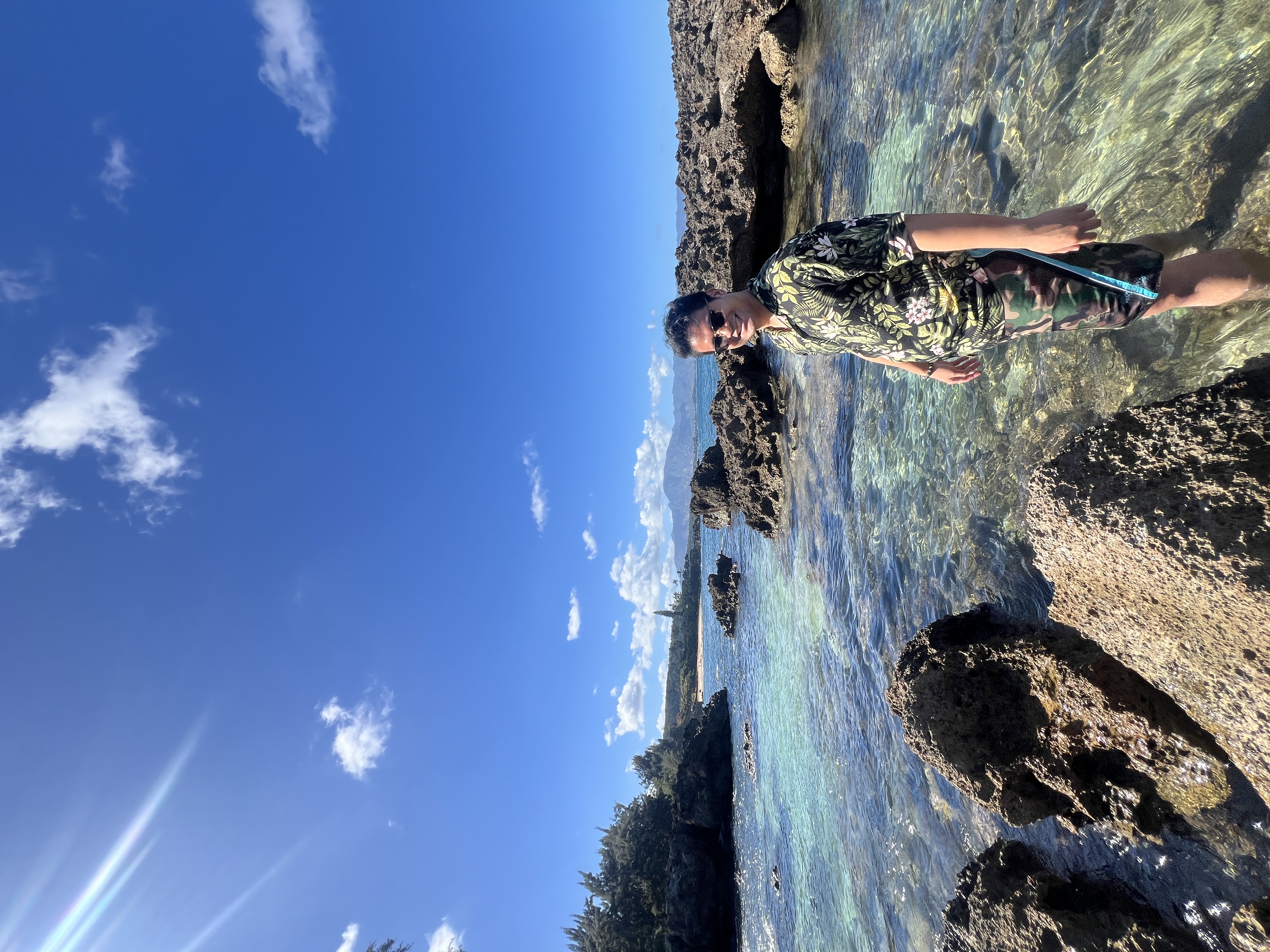Nico standing in clear shallow tide pools among dark rocks, mountains on the horizon.
