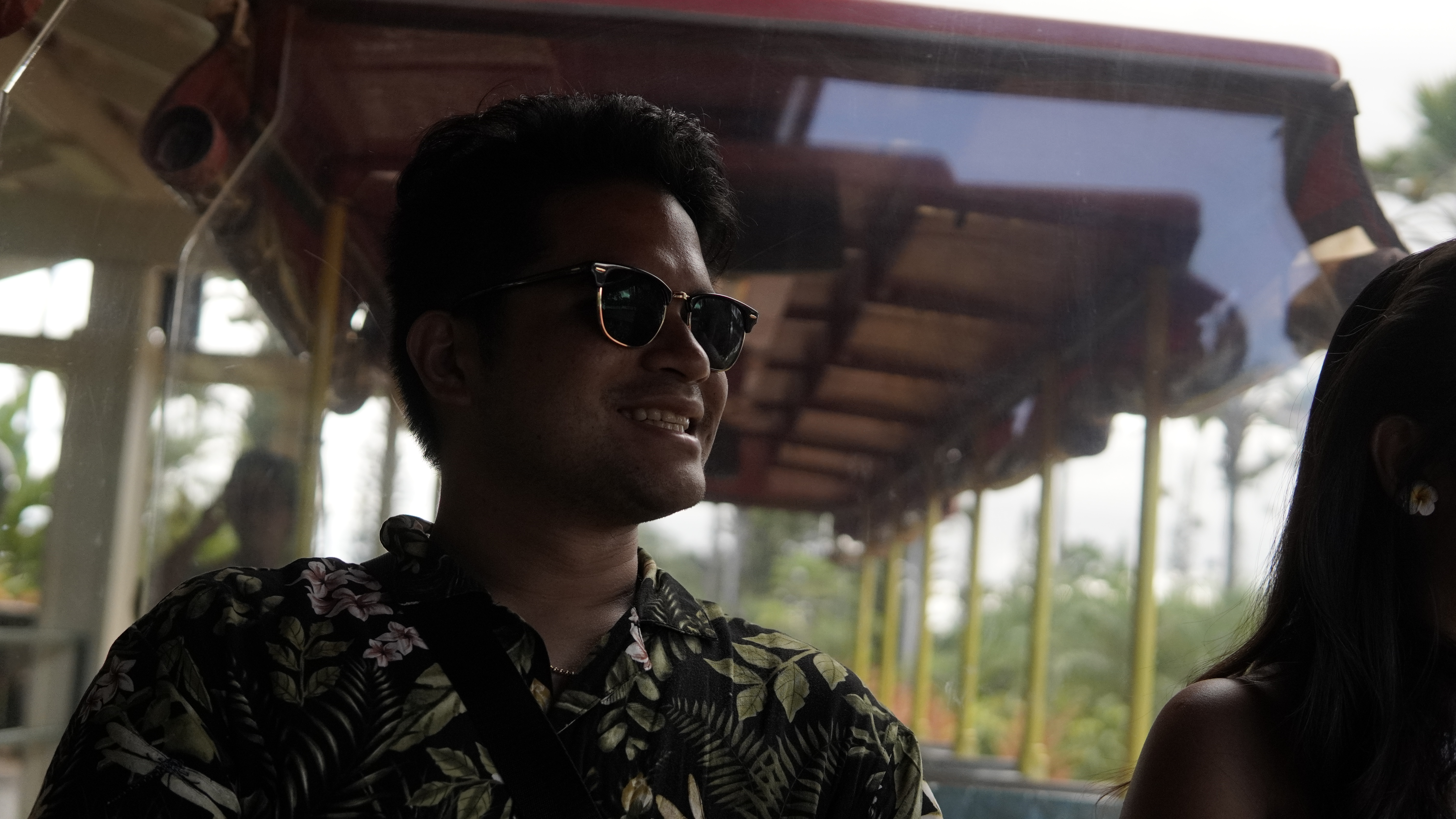Nico in sunglasses and a floral shirt, smiling under the red canopy of an open tram.