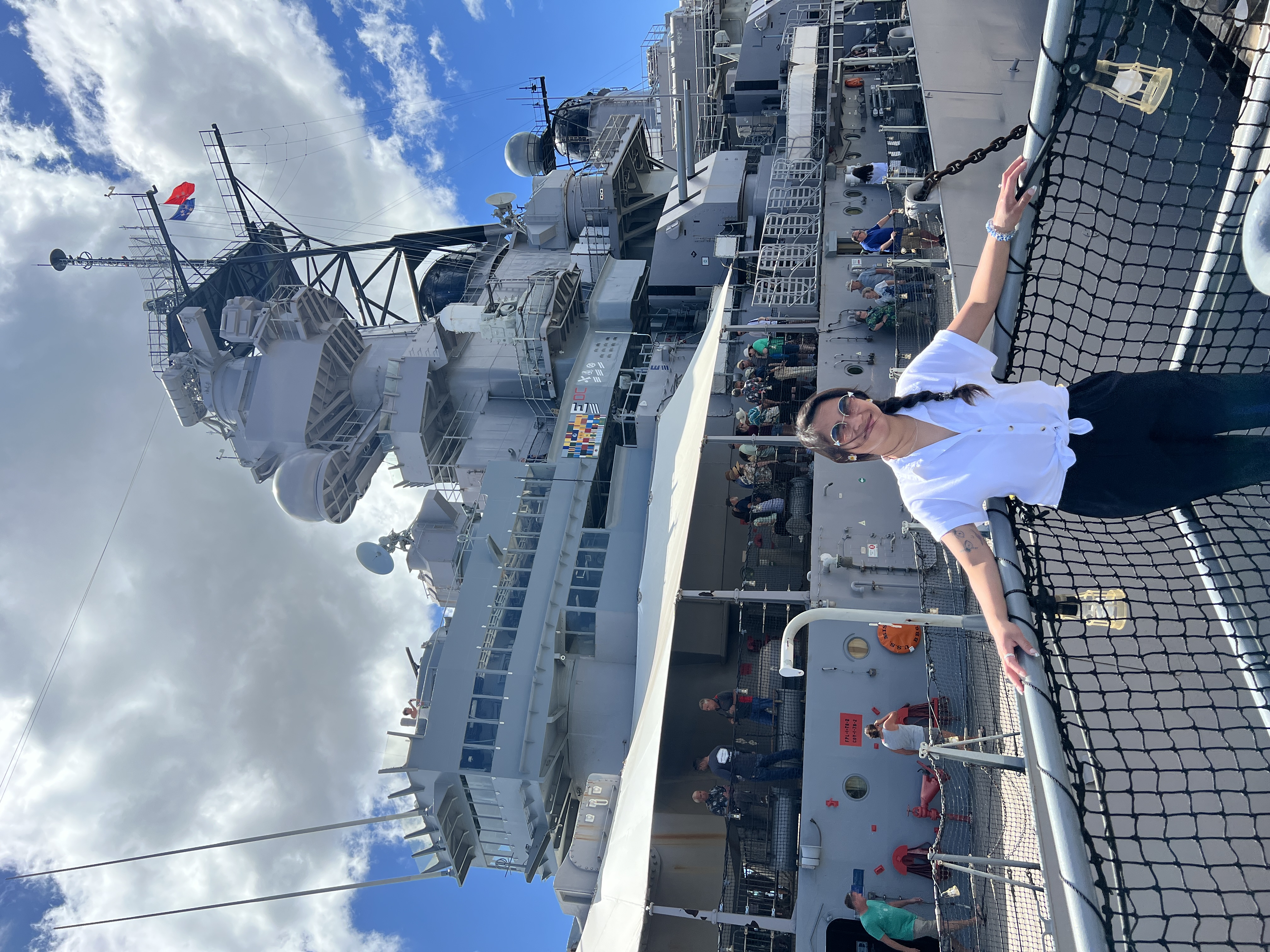 Sarah at the rail of the USS Missouri in a white shirt, arms out, the bridge and a flag rising behind her.