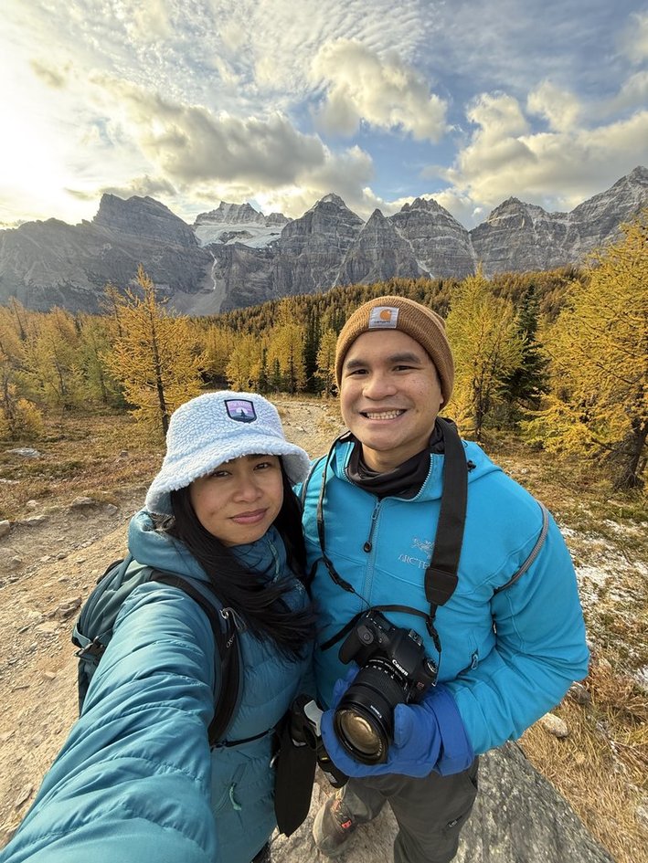 Selfie of the couple in warm gear with the golden larches and mountains behind them